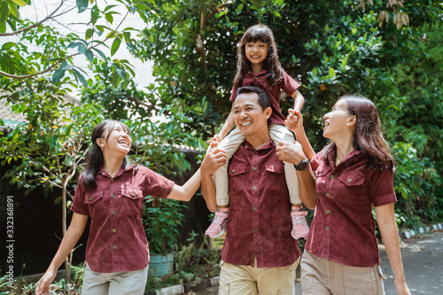 Asian family together walking outdoors holding hands and smiling father carrying on neck smiling daughter while walking in the park