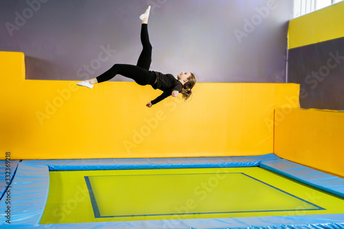 Young woman amateur acrobatic athlete jumping and exercising on a trampoline indoors, modern hobby and fitness concept