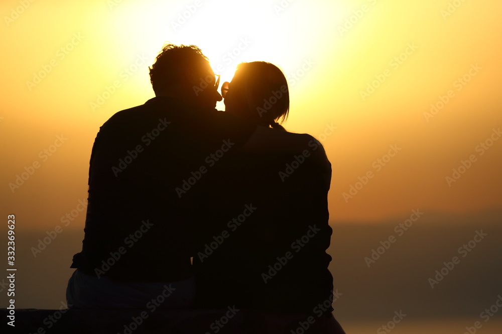 silhouette of couple in love embracing and kissing while enjoying the sunset