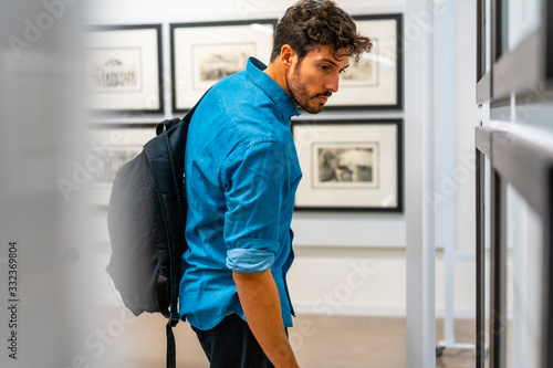 Lifestyle, a young Caucasian man looking at pictures from an exhibition in a denim jacket