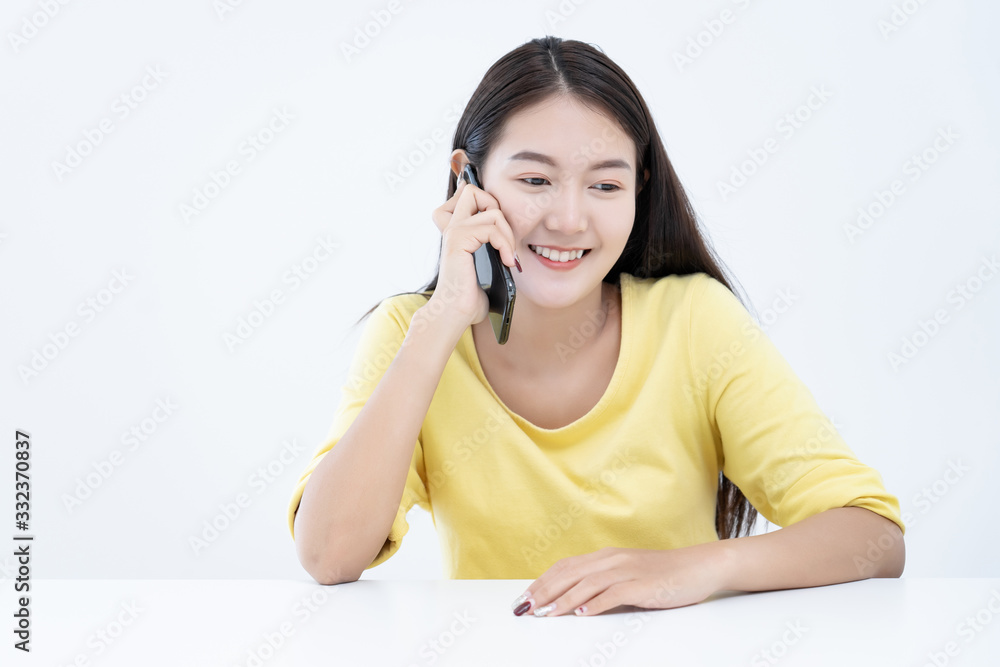Asian young woman ware yellow t-shirt using talking mobile phone or smart phone in white office room background Asian young woman ware yellow t-shirt using talking mobile phone or smart phone in white office room background