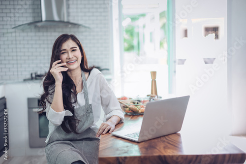 Image of young pretty woman standing in kitchen using computer laptop and cooking with the tomatoes and avocado. © Suntipong