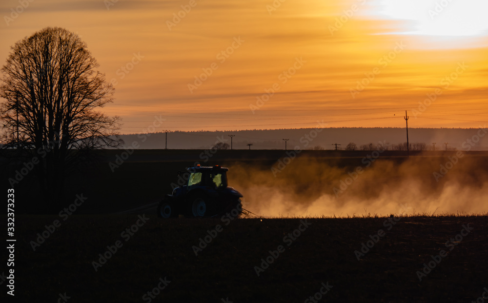 Fototapeta premium Tractor silhouette in the field on the orange-yellow sunset