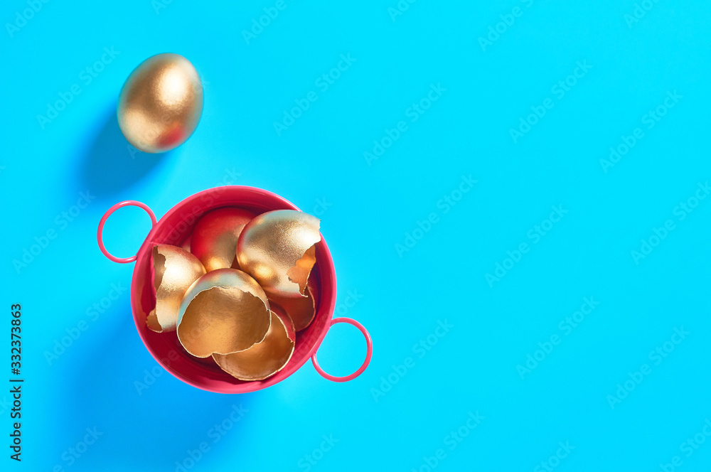 Red metal basin full of golden egg shells on blue background. Easter concept. Copy space. Top view