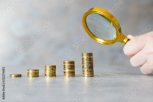 Lupa i rosnący stos monet. Koncepcja szukania oszczędności. © andsko