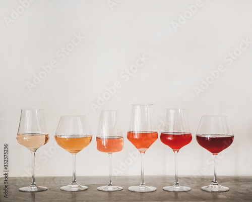 Fotografie, Obraz Various shades of Rose wine in stemmed glasses placed in line from light to dark colour on concrete table, white wall background behind, copy space