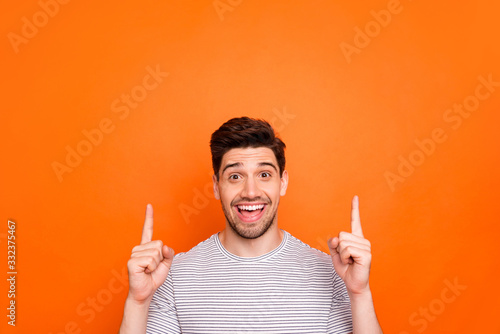 Closeup photo of attractive funny guy hold hands fingers direct up empty space excited good mood sales person nice offer wear striped t-shirt isolated bright orange color background