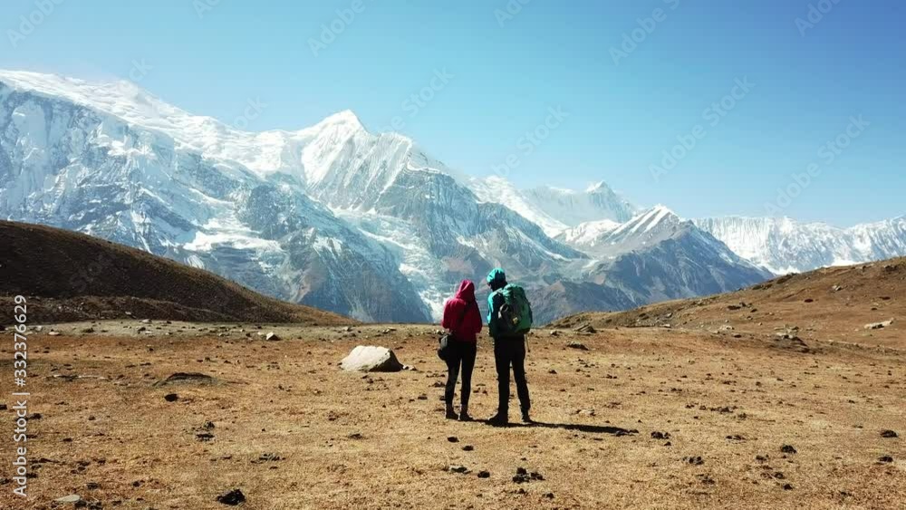 A couple enjoying the view form Ice lake, part of the Annapurna Circuit Trek, Himalayas, Nepal. Annapurna chain in the back, covered with snow. Clear weather, dry grass, snowy peaks. High altitude A couple enjoying the view form Ice lake, part of the Annapurna Circuit Trek, Himalayas, Nepal. Annapurna chain in the back, covered with snow. Clear weather, dry grass, snowy peaks. High altitude