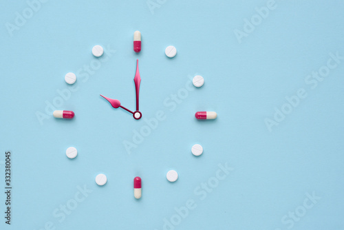 Clock created from pills and capsules on pastel blue background. Right time for using medicines. Flat lay. photo