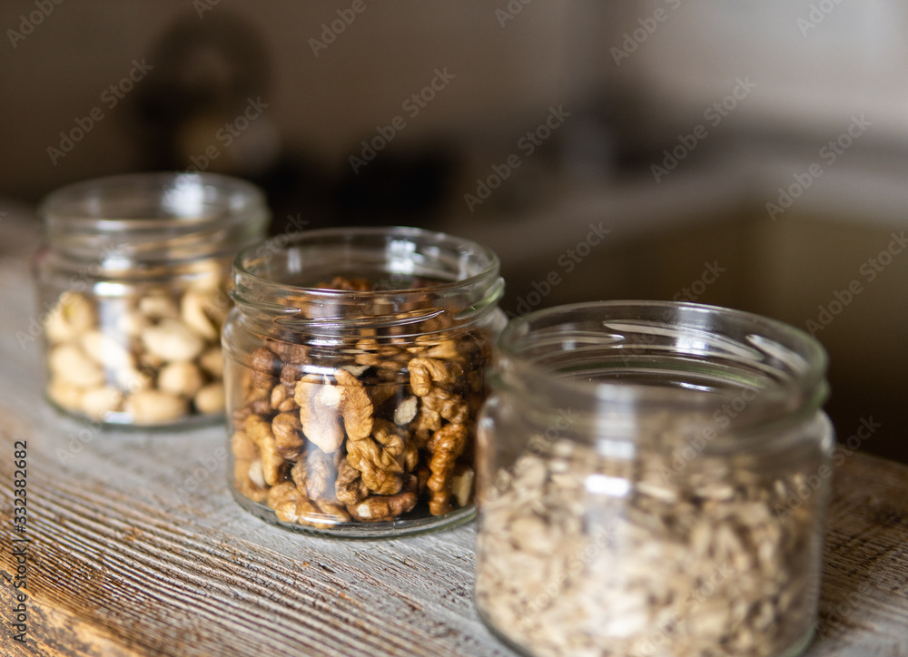 Sunflower seeds, walnut and pistachio in a jars which standing on a white vintage table with a kitchen on background. Nuts is a healthy vegetarian protein and nutritious food. Nuts on rustic old wood. Sunflower seeds, walnut and pistachio in a jars which standing on a white vintage table with a kitchen on background. Nuts is a healthy vegetarian protein and nutritious food. Nuts on rustic old wood.