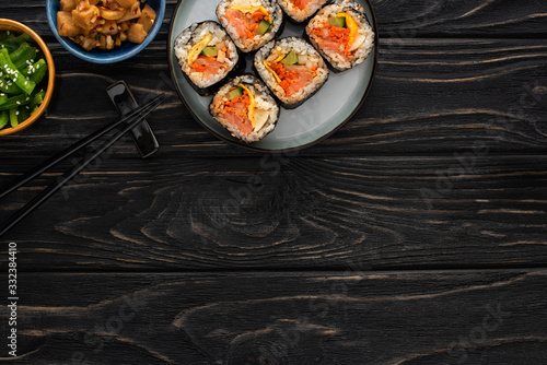 top view of chopsticks near plate with gimbap and korean side dishes on wooden surface