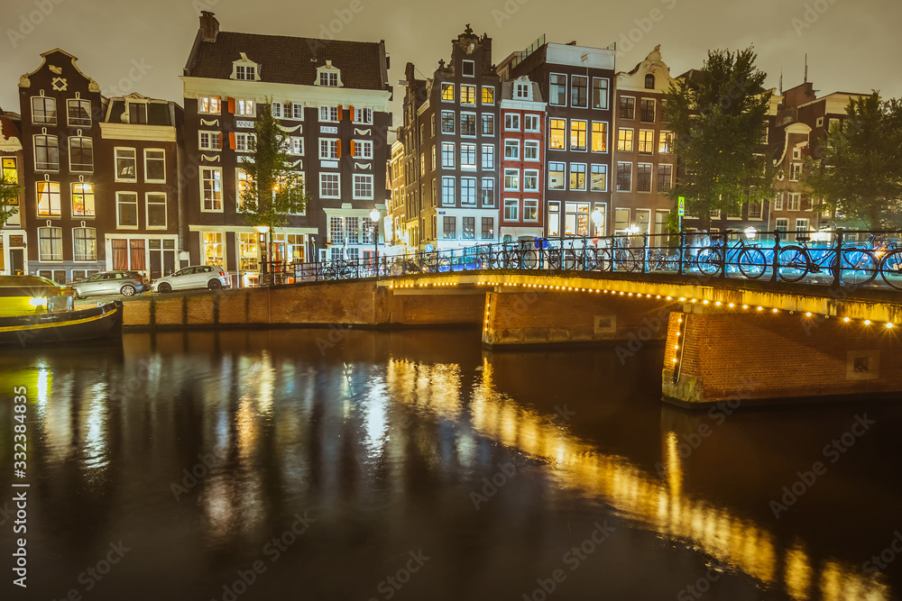 Panorama of Amsterdam canal Singel with typical dutch houses and bridge at night, Holland, Netherlands. Water in motion blur.
