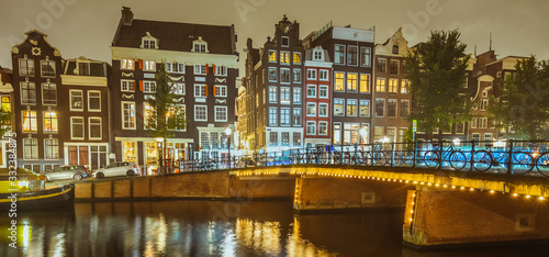 Panorama of Amsterdam canal Singel with typical dutch houses and bridge at night, Holland, Netherlands. Banner edition. Water in motion blur.