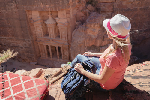 Woman traveler with backpack sitting on carpet viewpoint in Petra ancient city looking at the Treasury or Al-khazneh, famous travel destination of Jordan and one of seven wonders. 