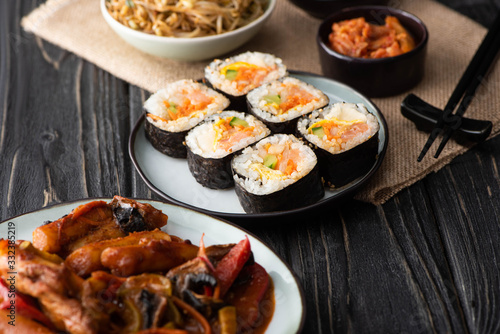 selective focus of gimbap with salmon near chopsticks on wooden surface