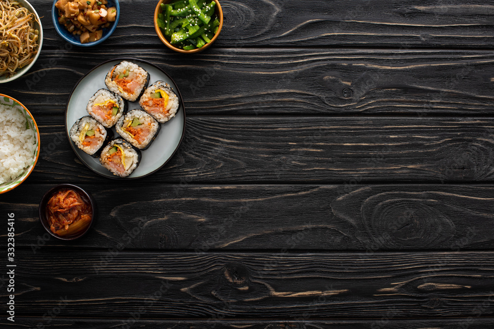 top view of bowls with korean side dishes near gimbap on wooden surface