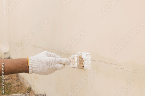 Close up of a hand with white cloth gloves that is being used to transform paint to seal the cracks on the concrete wall.