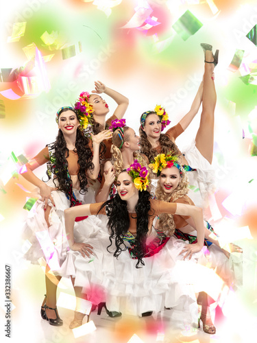 Surprised. Beautiful young women in carnival, stylish masquerade costume with feathers on white background in neon light, flying confetti. Holidays celebration, dancing, fashion. Festive time, party.