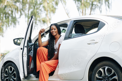 Beautiful young Black woman sitting in new car and showing electronic keys