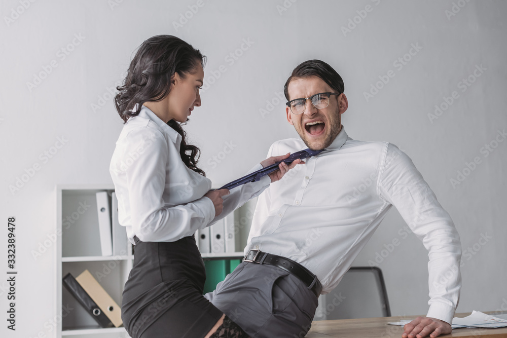 Obraz premium passionate businesswoman touching tie of shocked colleague while seductive him in office