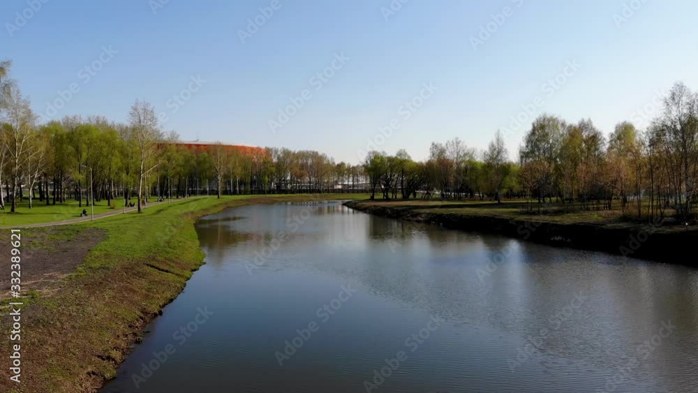 Aerial flight over the river flowing through the park. Spring weather, people walk and sit on benches. Aerial shot taken by drone in spring Aerial flight over the river flowing through the park. Spring weather, people walk and sit on benches. Aerial shot taken by drone in spring