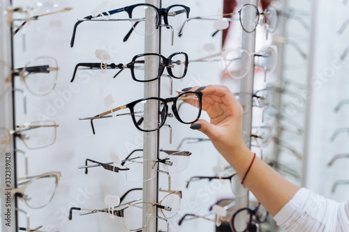 Eyeglasses shop. Stand with glasses in the store of optics. Womans hand chooses glasses.