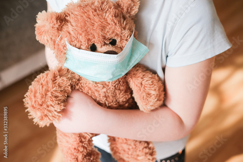little girl holding teddy bear in medical mask to protect from coronavirus.