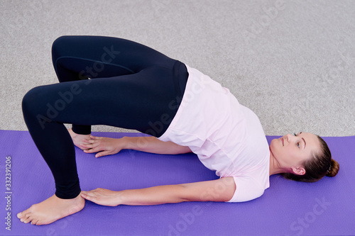Portrait of young woman practicing Kandharasana (shoulder pose) on mat at home indoor, copy space. Practicing yoga. Wellness and healthy lifestyle