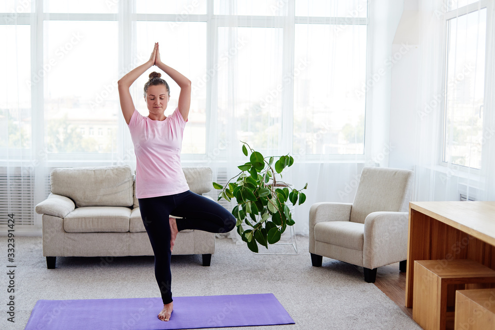 Portrait of young woman practicing balance yoga asana Vrikshasana at home indoor, copy space, back view. Girl doing tree pose, full length. Relaxing and doing yoga. Wellness and healthy lifestyle Portrait of young woman practicing balance yoga asana Vrikshasana at home indoor, copy space, back view. Girl doing tree pose, full length. Relaxing and doing yoga. Wellness and healthy lifestyle