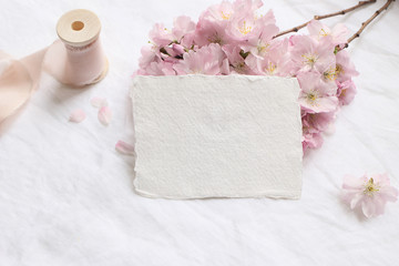 Wedding stationery mock-up scene. Blank greeting cards, envelope on linen tablecloth background with pink blossoming cherry tree branches and ribbon. Feminine still life composition. Flat lay,top view