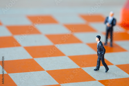 Miniature businessman walking on the orange chess game