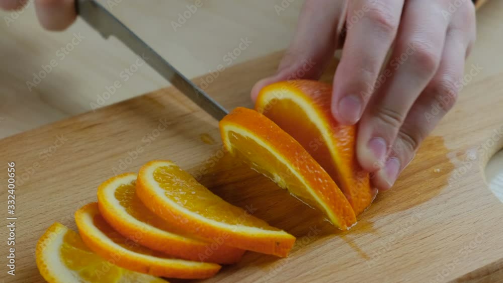 Hand cuts fresh orange into slices on a wooden board, close-up Hand cuts fresh orange into slices on a wooden board, close-up