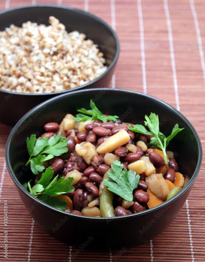Vegan low calorie lettuce with baked beans with carrots and greens and boiled buckwheat in black round bowls on brown straw mat front view Vegan low calorie lettuce with baked beans with carrots and greens and boiled buckwheat in black round bowls on brown straw mat front view