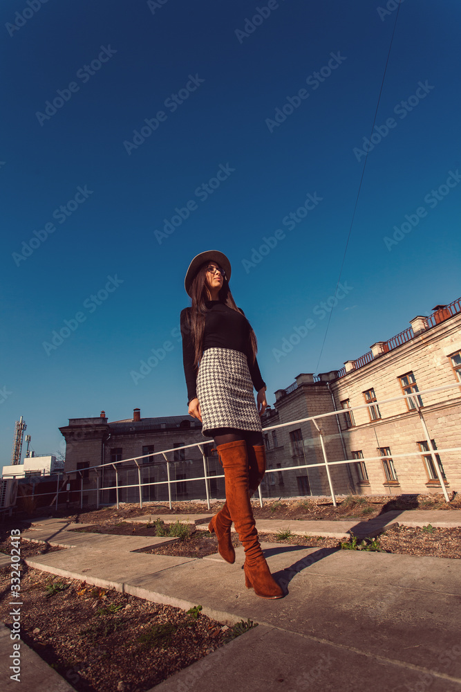Young pretty stylish girl walking along the street. Girl model in hat walks along the street.