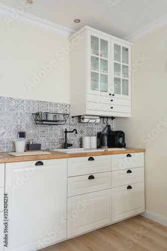 Cozy, bright Scandinavian-style kitchen. White, gray, black. Dishwashing sink, faucet, metal dishwasher, tile with patterns. © Olga