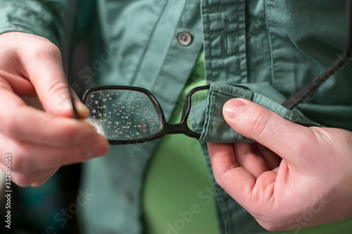 Bild auf Leinwand Male hand wiping raindrops with glasses, using shirt.