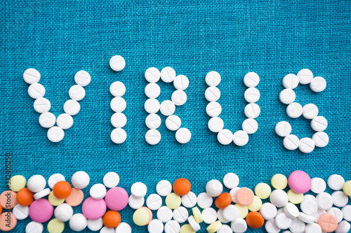 The inscription virus made of white capsules on a blue background. Below is a scattering of multi-colored tablets. The concept of the treatment of dangerous deadly coronavirus. Free space