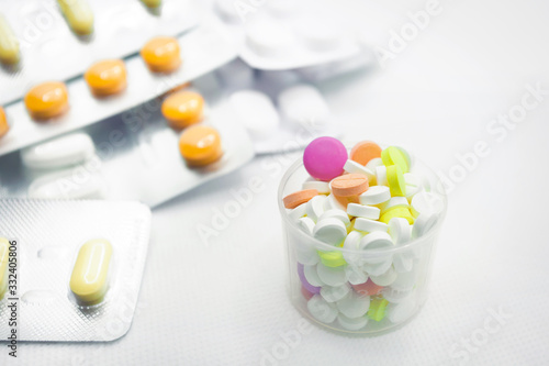 The concept of pills for treatment. Multi-colored pills in blisters on a white isolate. In a measuring glass in bulk, tablets of different colors. A serving of pills for today. Daily dose.