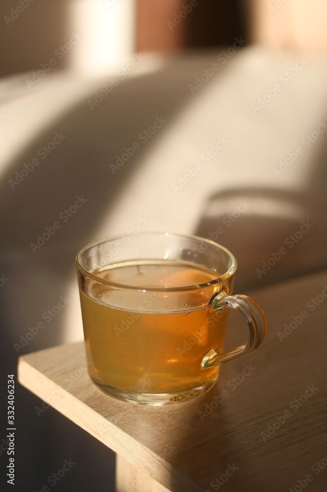 Cup of herbal tea on a living room table, illuminated by sunlight. Selective focus.