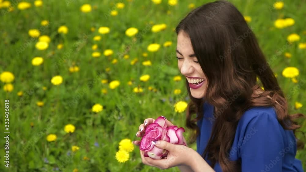 Fashionable girl in blue dress is sniffing the rosebud in the blooming forest. Beautiful fashionable woman with long hair in blue dress is sniffing the rosebud in the blooming forest Fashionable girl in blue dress is sniffing the rosebud in the blooming forest. Beautiful fashionable woman with long hair in blue dress is sniffing the rosebud in the blooming forest