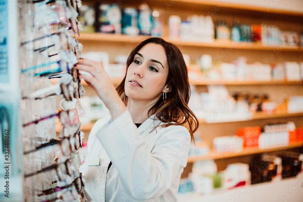 .Young female pharmacist working in her large pharmacy. Placing medications and glasses, taking inventory. Lifestyle