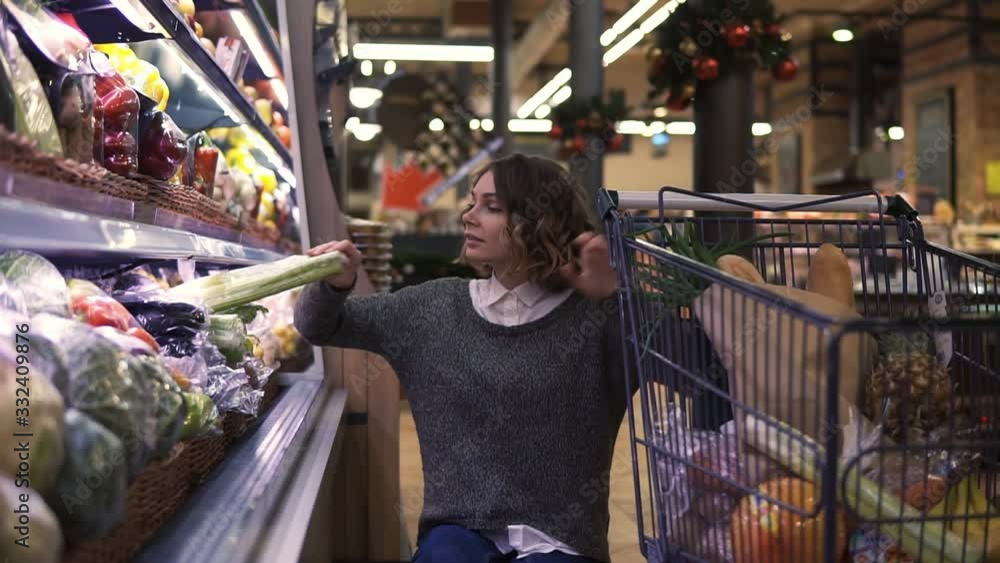 Young woman in modern supermarket choosing celery leek in organic vegetable department. Healthy female buying green food. Concept fresh, assortment, vegetarian girl in grocery store Young woman in modern supermarket choosing celery leek in organic vegetable department. Healthy female buying green food. Concept fresh, assortment, vegetarian girl in grocery store