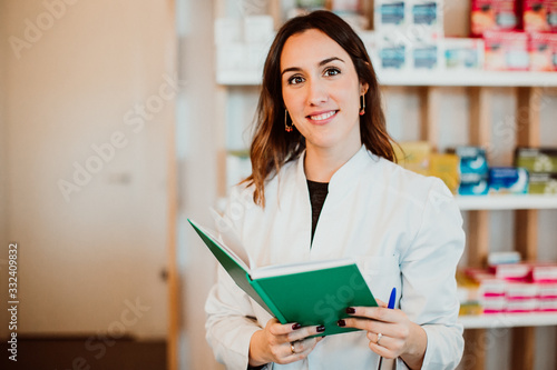 .Young female pharmacist working in her large pharmacy. Placing medications, taking inventory with her green notebook. Lifestyle