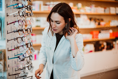 .Young female pharmacist working in her large pharmacy. Placing medications and glasses, taking inventory. Lifestyle