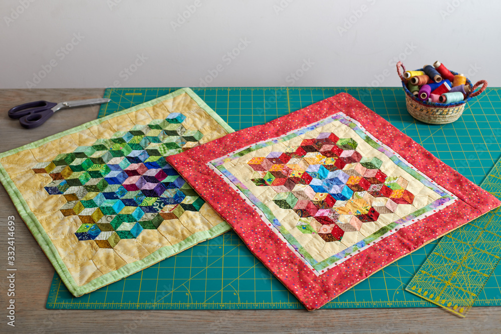 Fototapeta premium Mini quilts, basket with spools of thread, tools for patchwork and sewing on cutting mat