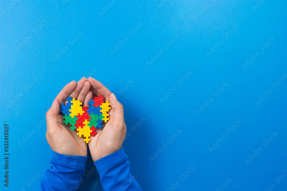 World autism awareness day concept. Child hands holding colorful puzzle heart on blue background World autism awareness day concept. Child hands holding colorful puzzle heart on blue background