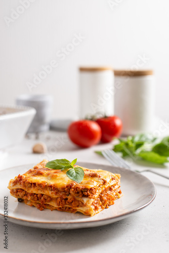 Tomato and ground beef lasagne with cheese and tomatoes layered between sheets of traditional Italian pasta served on a gray plate. Italian menu recipe. Side view, copy space. Tasty homemade lasagna