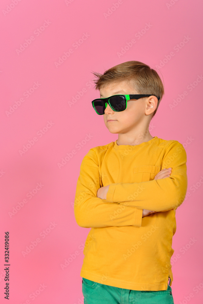 Glamorous and stylish boy posing for the camera, model in sunglasses, in yellow clothes in the studio on a pink background. Glamorous and stylish boy posing for the camera, model in sunglasses, in yellow clothes in the studio on a pink background.