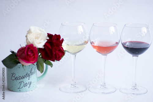 PInk, red, white wine in glasses and roses in cup on white background