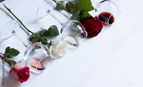 Laying glasses with red  pink  white wine and colorful rose flowers on light background